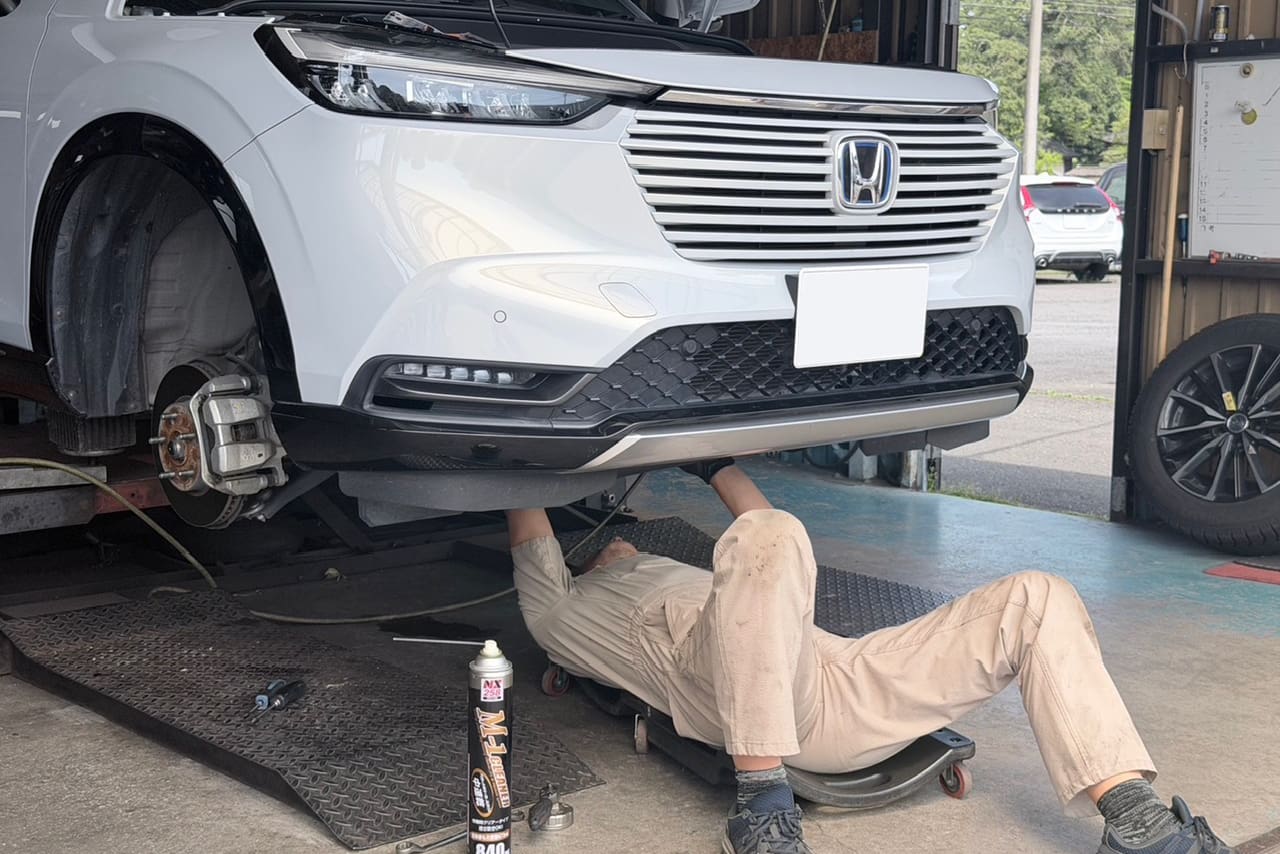 リフトアップされた車の下回りを点検する整備士