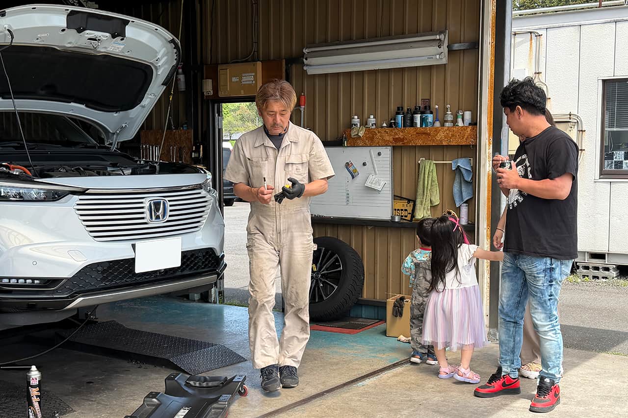 ガレージ内で小さな子供を連れたお客様と笑顔で話す整備士